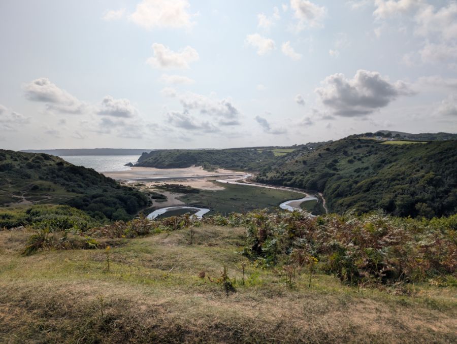 A green headland opening to a sandy bay and the sea
